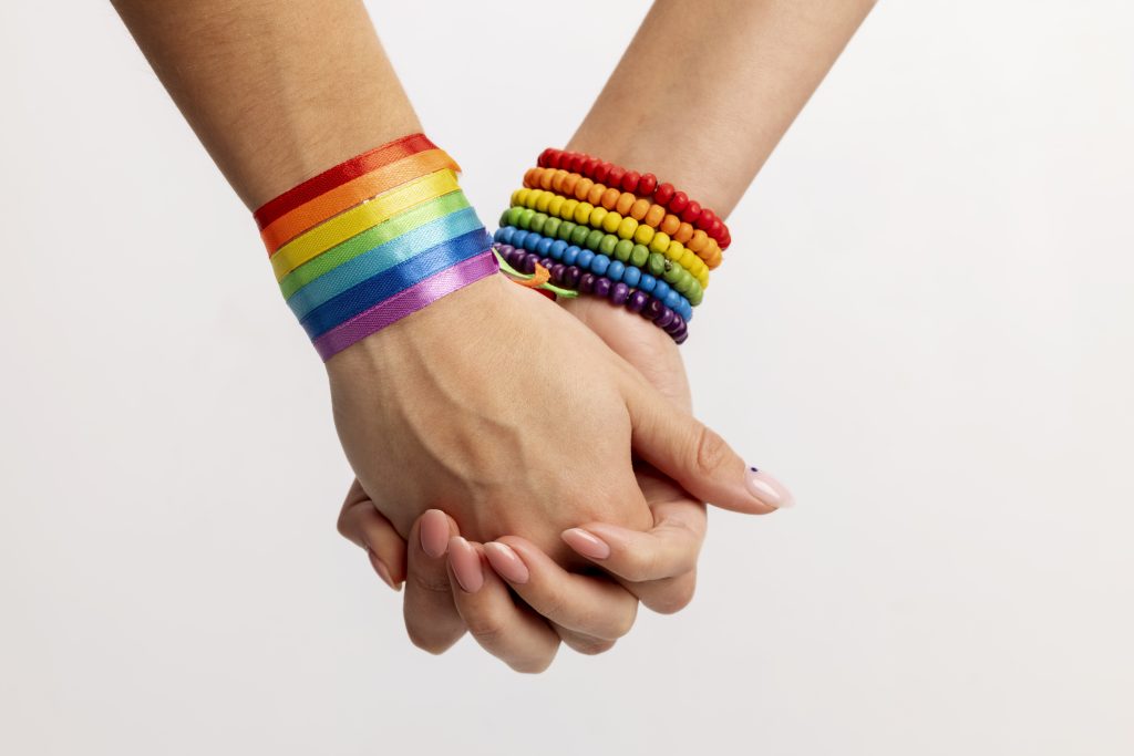 Dos mujeres se cogen de la mano con unas pulseras con los colores de la bandera LGTBI